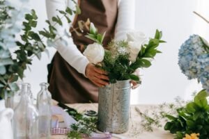 Crop anonymous female decorating metal bucket with fresh gentle white roses in blossom on blurred background