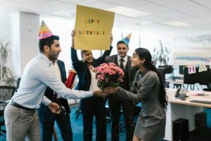 Happy office birthday celebration with colleagues exchanging gifts and wearing party hats.